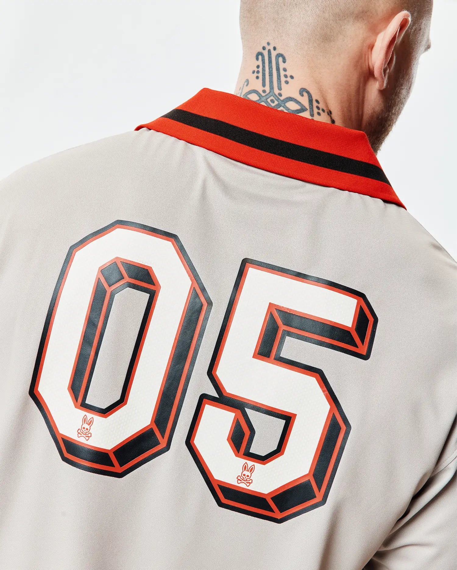 Mens Camden Oversized Soccer Jersey in light grey, with orange/black striped ribbed collar. Back features large 3D 05 numbers in white/black/orange, small orange Psycho Bunny skull logo within. (2)