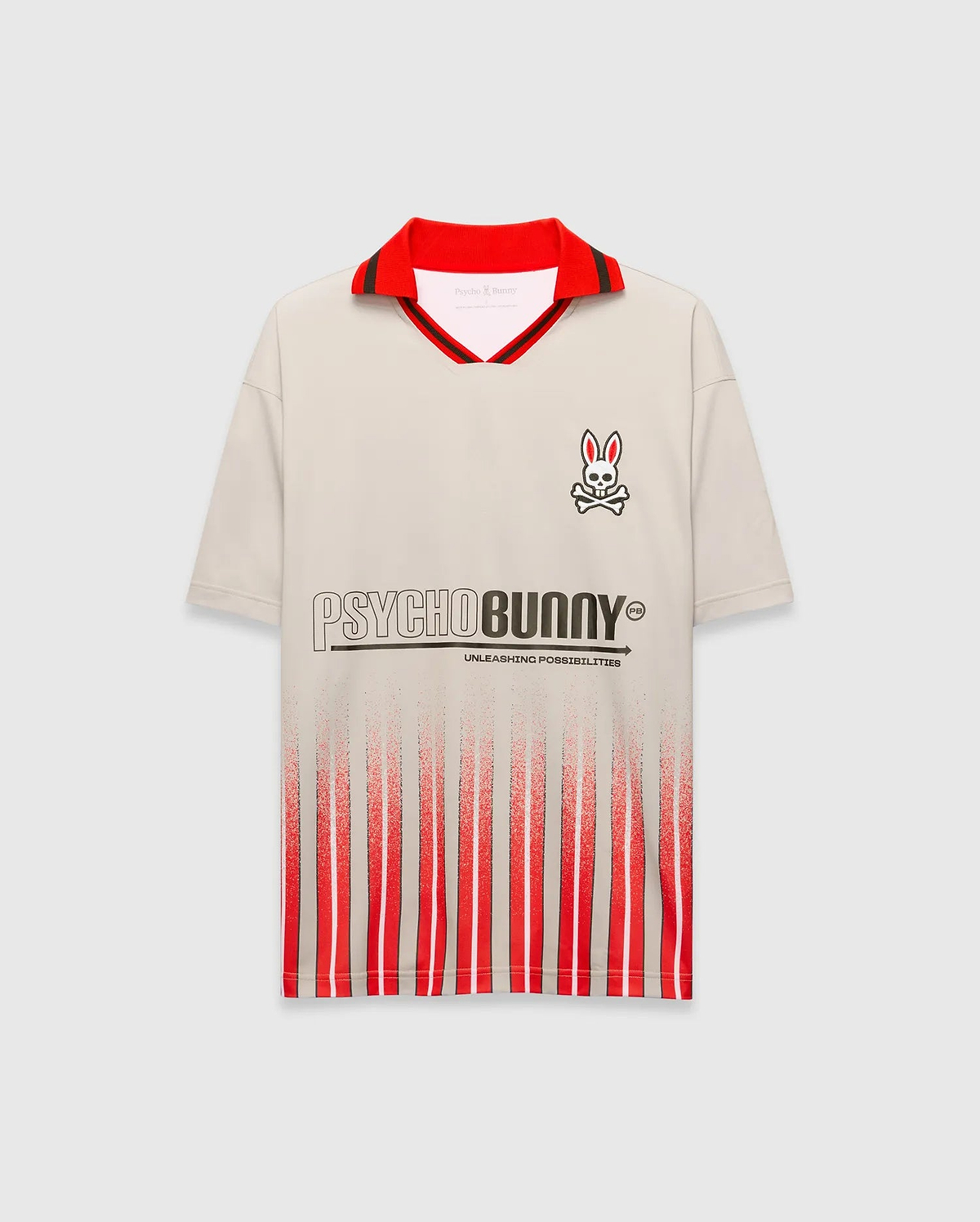 Mens Camden Oversized Soccer Jersey in beige, with a red polo collar, black stripe, small right chest Psycho Bunny skull logo, large PSYCHOBUNNY graphic, and red/black distressed vertical stripes. (5)