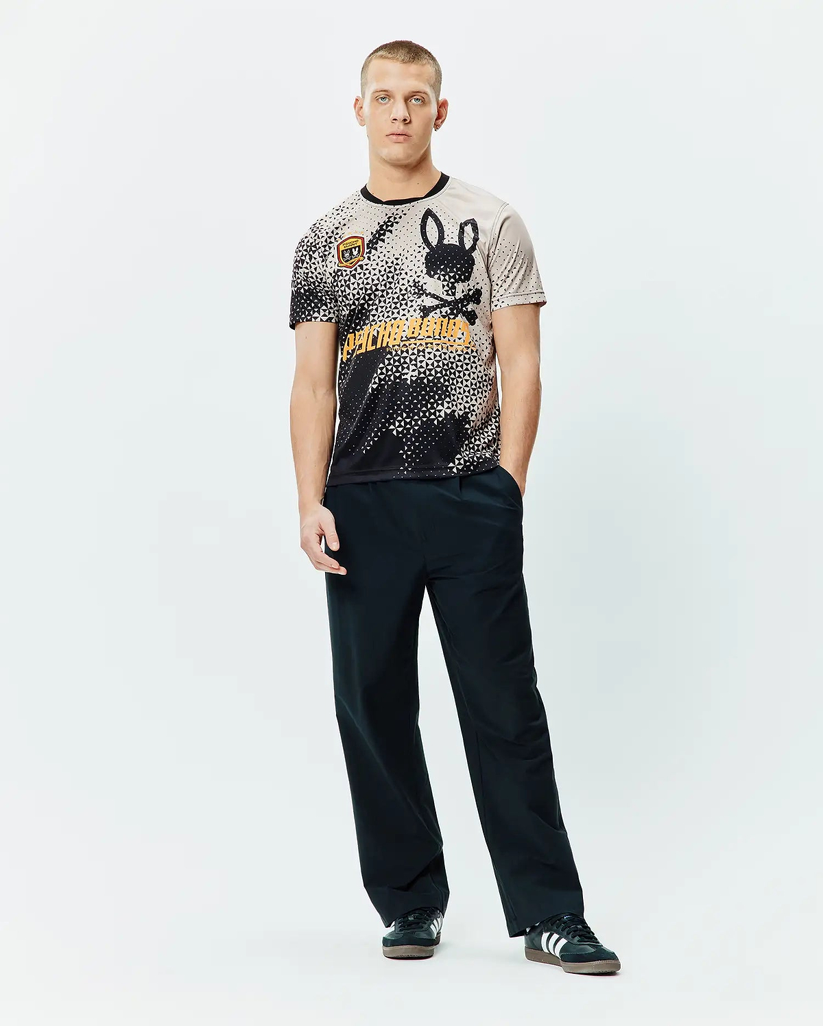 Mens Joshua Soccer Tee featuring a black and beige pixelated gradient, large black bunny skull logo, bold orange Psycho Bunny text, and a small shield patch on a classic fit jersey knit. (4)