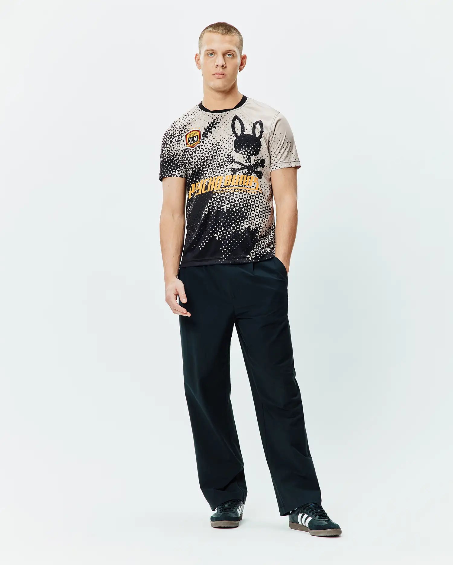 Mens Joshua Soccer Tee featuring a black and beige pixelated gradient, large black bunny skull logo, bold orange Psycho Bunny text, and a small shield patch on a classic fit jersey knit. (4)