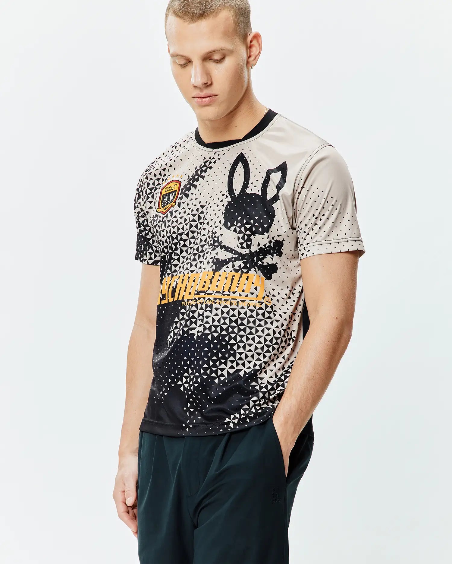Mens Joshua Soccer Tee with a black and beige geometric pattern, large black Psycho Bunny skull and crossbones graphic, yellow brand text, and a small embroidered patch logo on the sleeve. Smooth jersey, classic fit. (1)