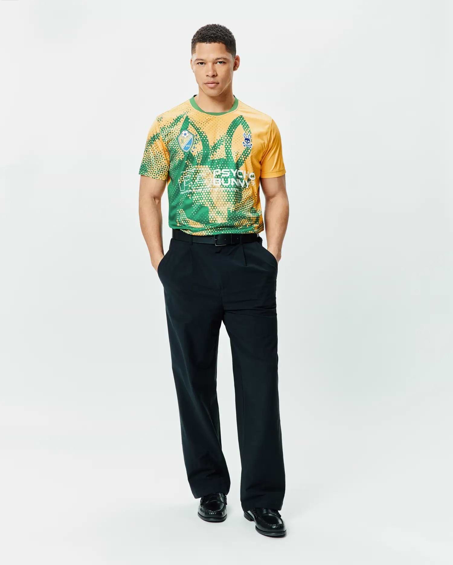Mens Joshua Soccer Tee in gold and green geometric pattern, featuring a large PSYCHO BUNNY graphic and small blue bunny skull logo on the left chest, classic fit performance jersey. (5)