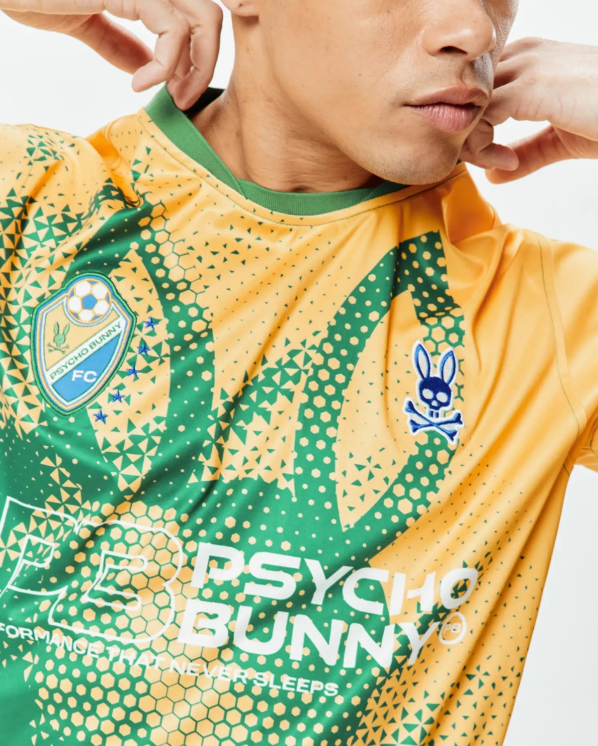 Mens Joshua Soccer Tee, gold and emerald green performance jersey with a geometric gradient pattern. Features an embroidered Psycho Bunny FC shield, blue bunny skull logo, and large PSYCHO BUNNY text. (3)