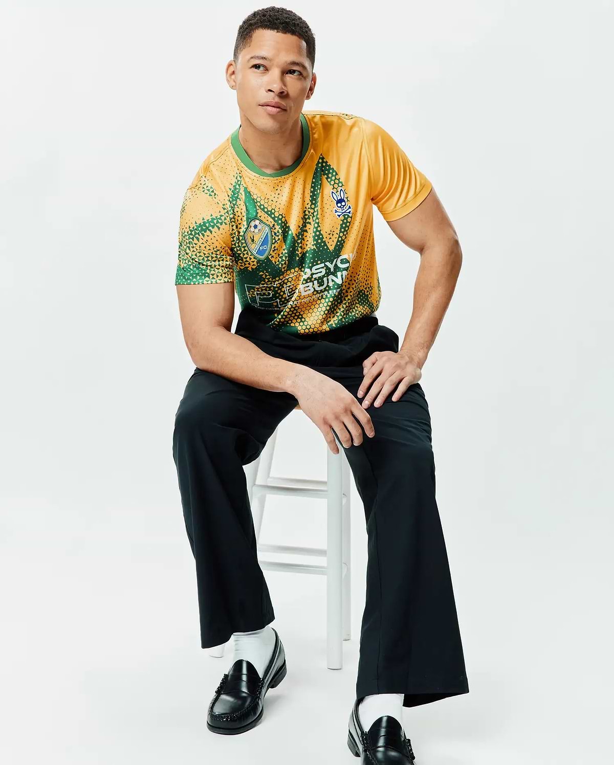 Mens Joshua Soccer Tee in yellow and green geometric dot pattern, featuring a blue Psycho Bunny skull logo on the right chest, an FC logo on the left chest, and large Psycho Bunny text on the front. Classic fit, smooth jersey. (4)