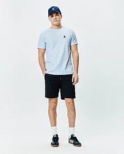 Light blue Mens Taylor Pique Tee with a classic fit and small embroidered Psycho Bunny skull logo on the left chest, paired with a navy cap and black shorts.