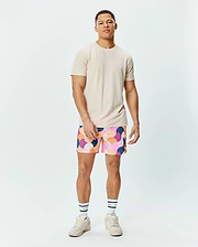 Mens Taylor Pique Tee in light beige with a small embroidered white Psycho Bunny logo on the left chest, paired with multi-color abstract patterned shorts featuring a black bunny logo on the right thigh.