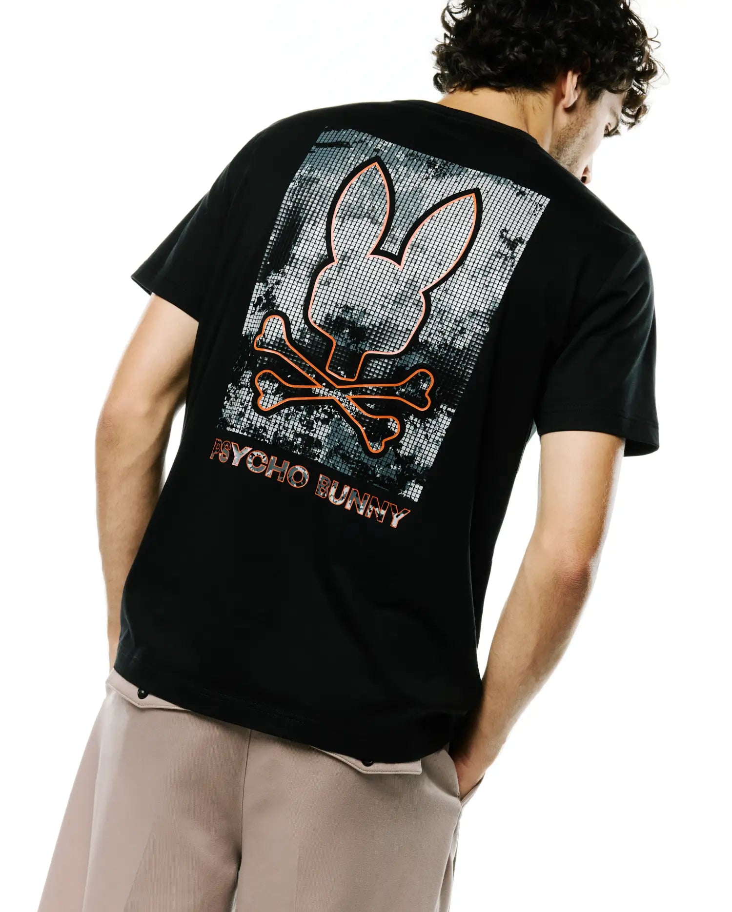 Black classic fit jersey t-shirt with a large back graphic featuring an orange outlined Psycho Bunny skull and crossbones over a grey pixelated background, with PSYCHO BUNNY text below. Men's Alfie Back Graphic Tee. (1)