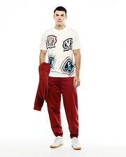 Men's Klaus Jacquard Tee in cream, a relaxed fit jersey t-shirt with multiple iconic distorted red, light blue, and dark blue Psycho Bunny skull logos. Styled with relaxed deep red french terry sweatpants and a matching hoodie. (4)