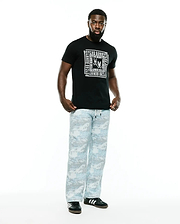 Black Men's Raj Wordmark Graphic Tee, classic fit, with a large white Psycho Bunny repeating wordmark and skull logo chest graphic. Paired with relaxed light blue and grey digital camo pants. (5)