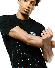 Mens Malcolm Graphic Tee, a black jersey knit t-shirt with a classic fit, featuring a white PSYCHO BUNNY text logo on the chest and a vibrant white, teal, and dark blue paint splatter graphic on the lower half.