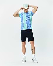 Mens Blaze Sport Tee in vibrant blue and teal wavy swirl pattern, with a small white Psycho Bunny chest logo. Paired with black athletic shorts and a mint green cap with an embroidered bunny skull. (4)