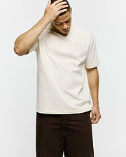 Mens Windcrest Relaxed Fit Tee in cream smooth jersey, featuring a large tonal embossed PSYCHO BUNNY text logo centered on the chest and a small black side seam tag. (3)
