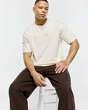 Mens Windcrest Relaxed Fit Tee in cream, featuring a smooth jersey fabric and a large, tonal embroidered Psycho Bunny text logo on the center chest. (1)