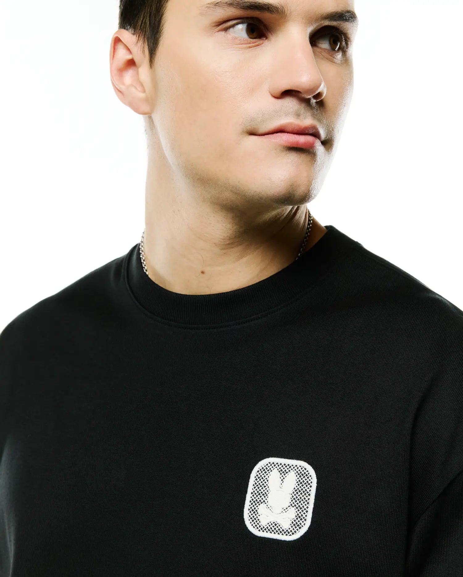 Men's Samson Oversized Bunny Tee in black jersey knit, featuring a small white embroidered Psycho Bunny skull logo patch with a mesh background on the left chest. (2)