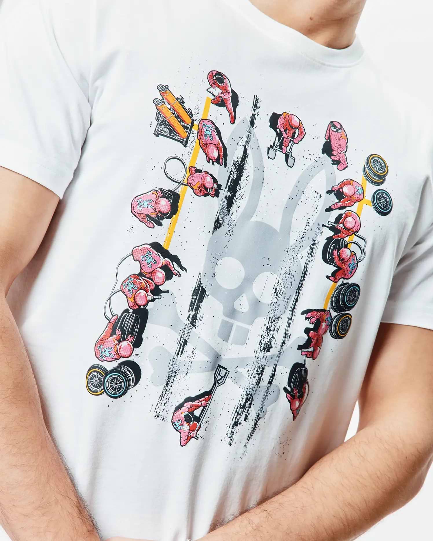 Mens Race Bunny Graphic Tee. White classic fit jersey t-shirt featuring a large distressed grey Psycho Bunny skull graphic surrounded by pink pit crew figures, yellow lines, and black grunge details.