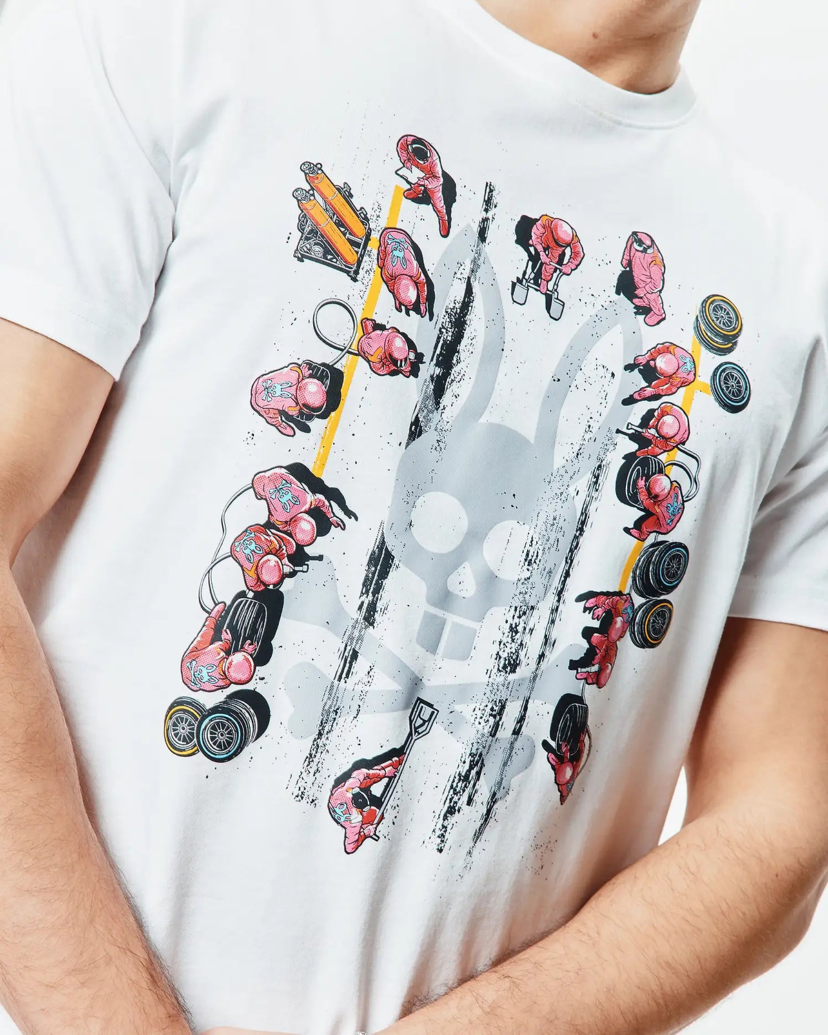Mens Race Bunny Graphic Tee. White classic fit jersey t-shirt featuring a large distressed grey Psycho Bunny skull graphic surrounded by pink pit crew figures, yellow lines, and black grunge details.