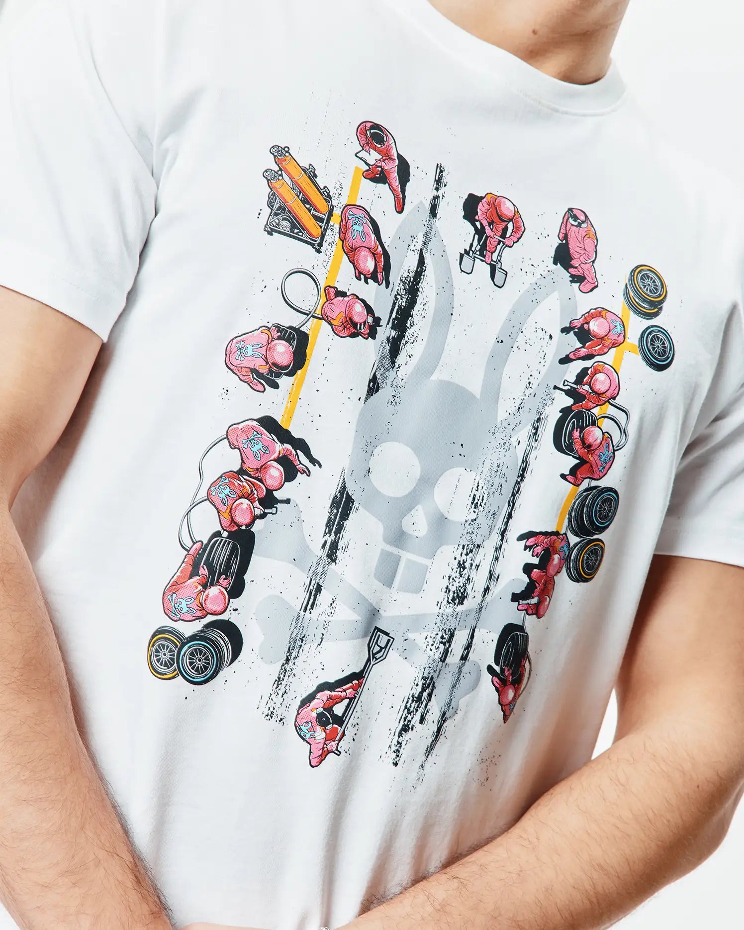 Mens Race Bunny Graphic Tee. White classic fit jersey t-shirt featuring a large distressed grey Psycho Bunny skull graphic surrounded by pink pit crew figures, yellow lines, and black grunge details.