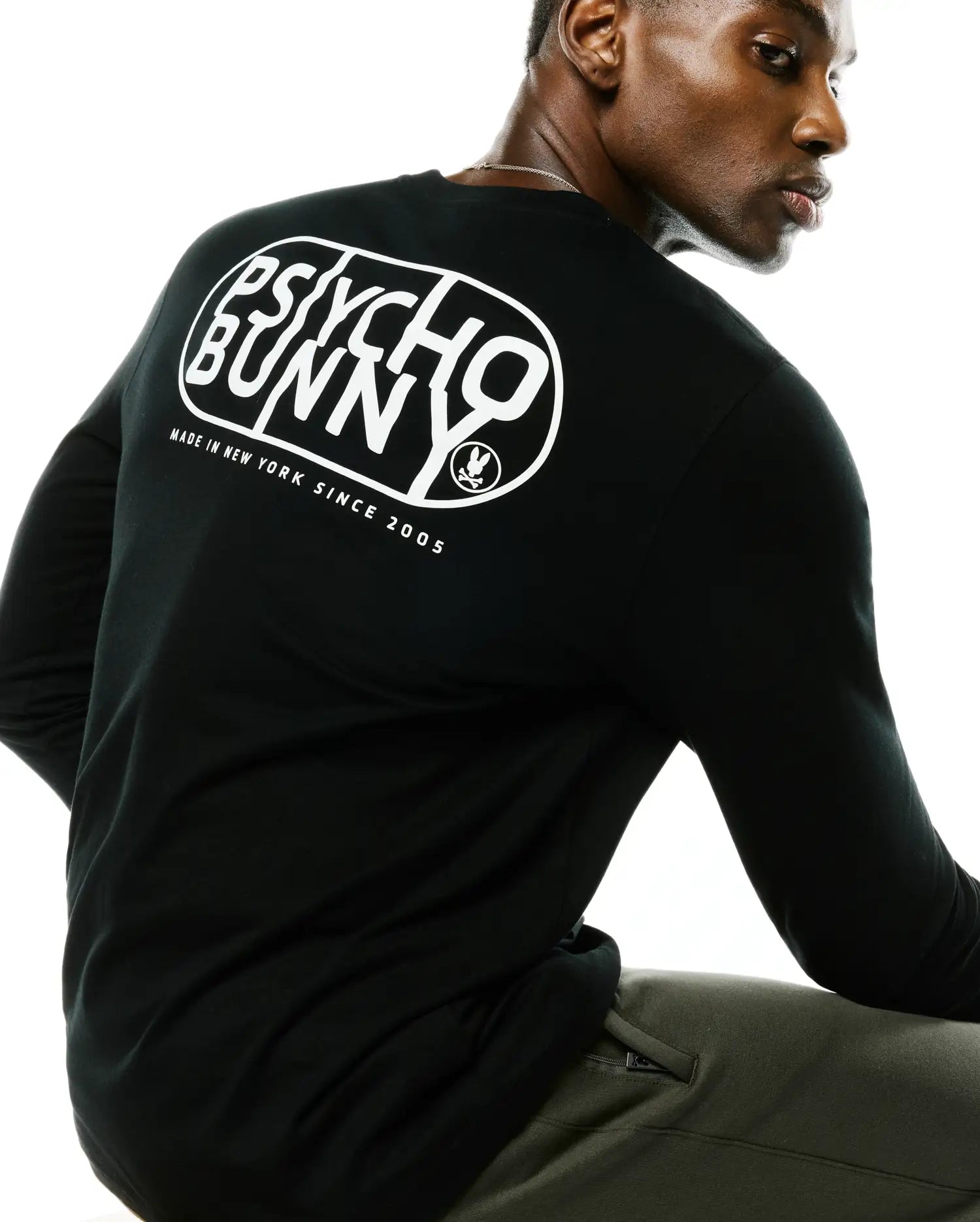 Black Mens Dariel Long Sleeve Back Graphic Tee in soft jersey knit, featuring a large white Psycho Bunny oval graphic on the back with Made In New York Since 2005 text and the iconic bunny skull logo.