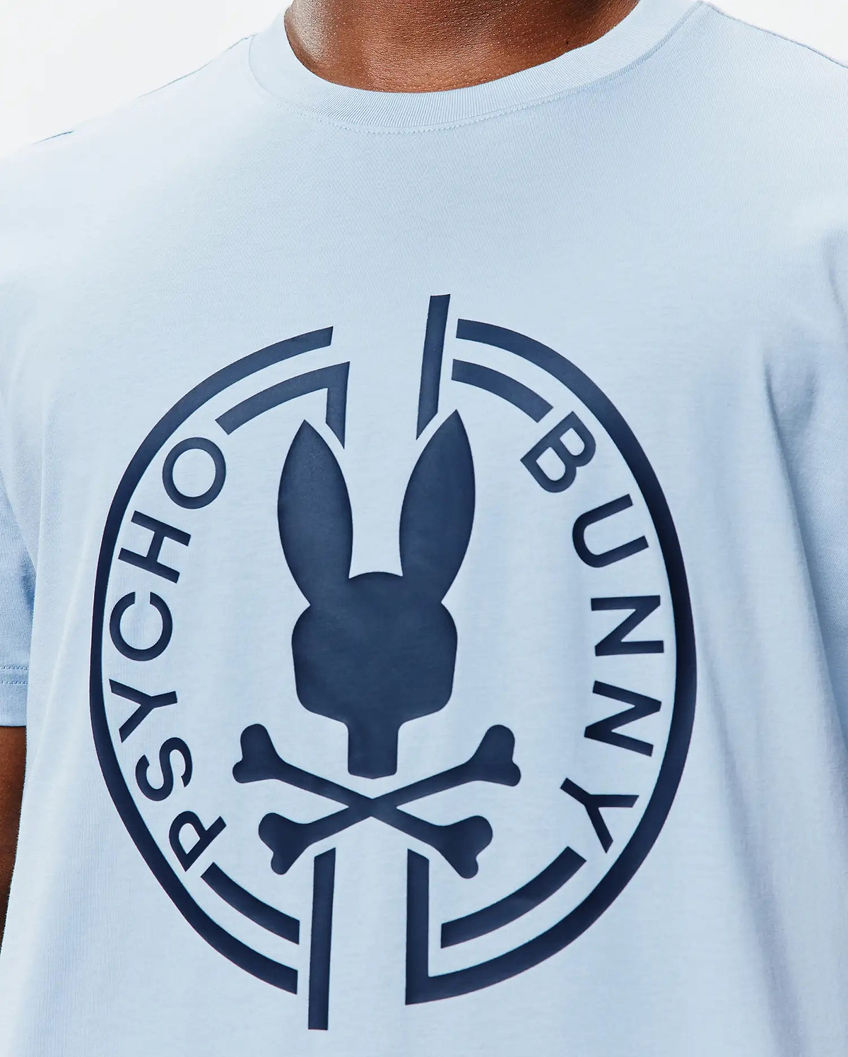 Mens Santa Fe Bunny Graphic Tee, a light blue jersey knit t-shirt with a classic fit, featuring a large navy Psycho Bunny skull and crossbones logo graphic on the central chest, encircled by PSYCHO BUNNY text. (3)