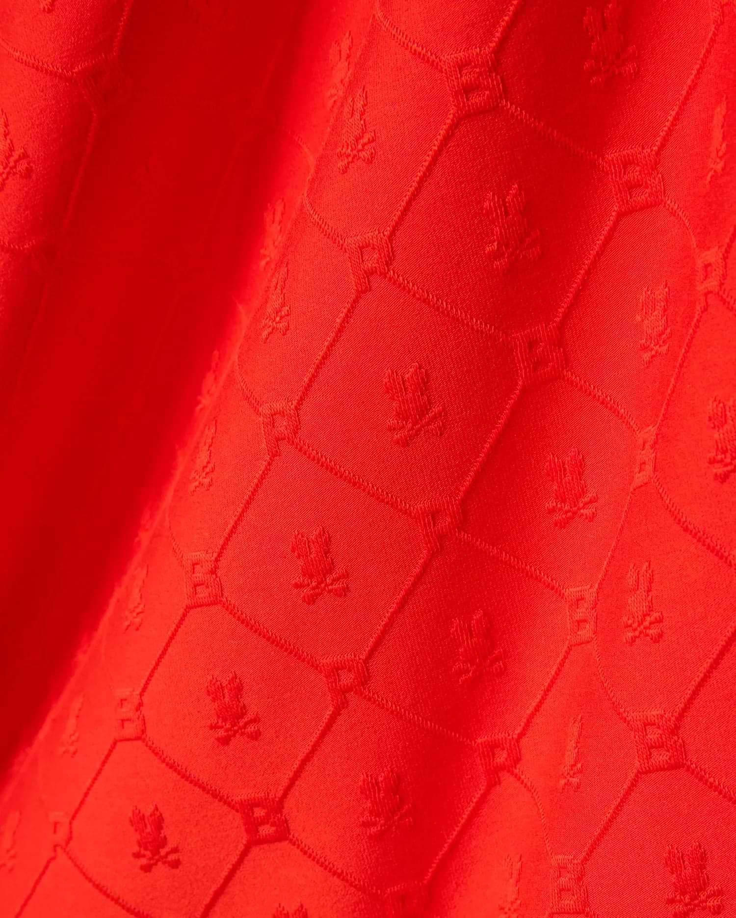 Bright red Mens Garry Relaxed Fit Tee featuring a subtle, all-over tonal jacquard pattern of the iconic Psycho Bunny skull logo within a textured geometric grid. (6)