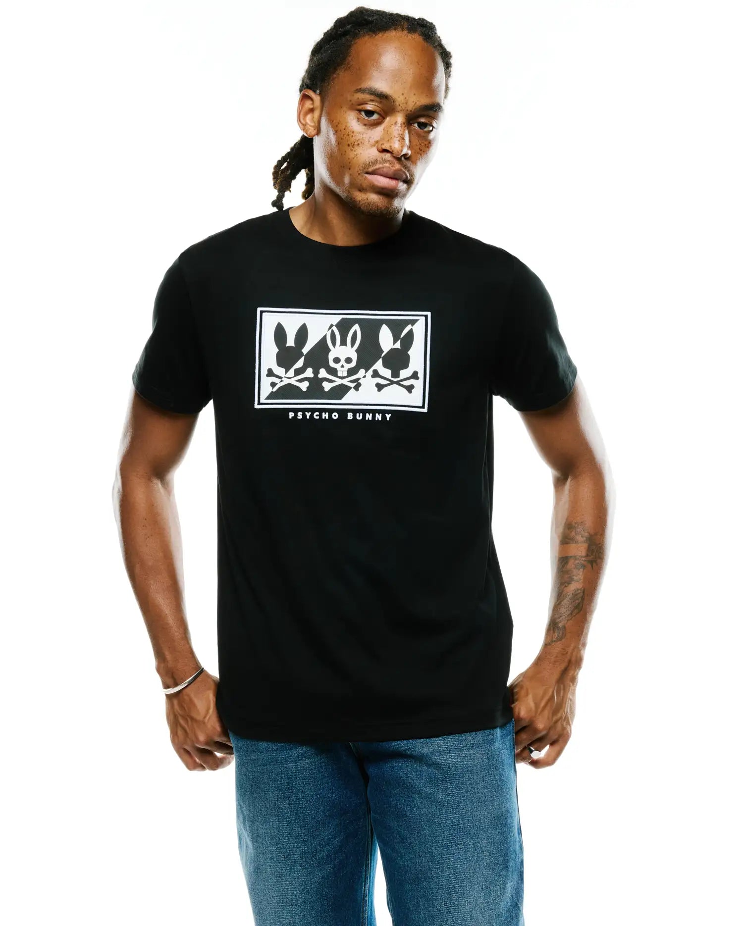 Mens Desmond Graphic Tee, black classic fit jersey t-shirt with a large white chest graphic featuring three Psycho Bunny skull logos, crossbones, and PSYCHO BUNNY text in a rectangular border.