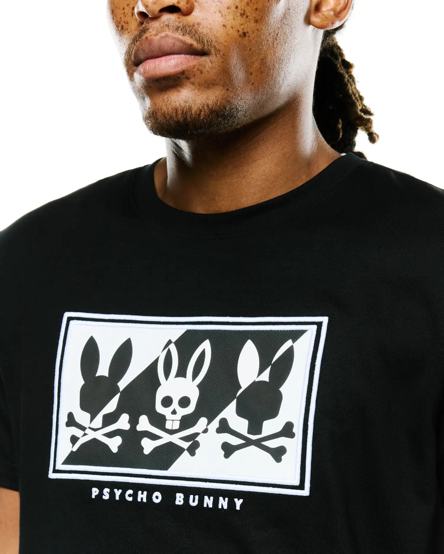 Mens Desmond Graphic Tee, black classic fit jersey, featuring a large chest graphic with three stylized white and black Psycho Bunny skull logos in a checkerboard pattern, bordered by white embroidery and Psycho Bunny text.