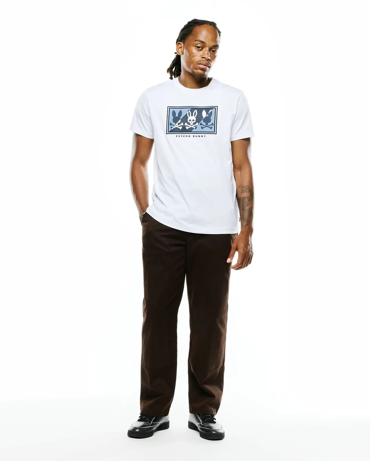 Mens Desmond Graphic Tee, a white classic fit jersey t-shirt featuring a large center chest graphic of multiple blue and grey Psycho Bunny skull logos in a rectangular frame with Psycho Bunny text.