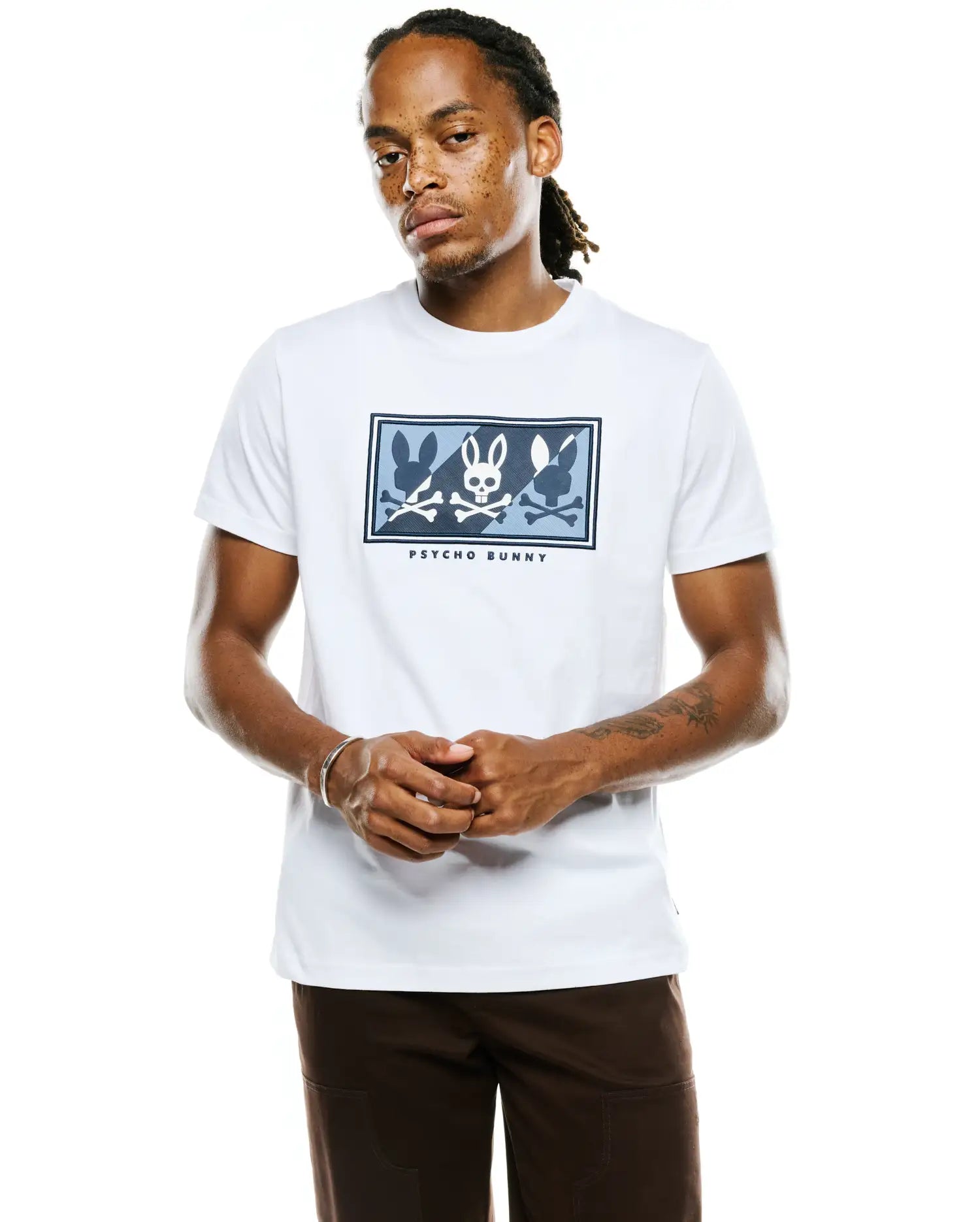 Mens Desmond Graphic Tee, a classic fit white jersey t-shirt featuring a large central chest graphic with blue and light blue bunny skulls and silhouettes, plus Psycho Bunny text.