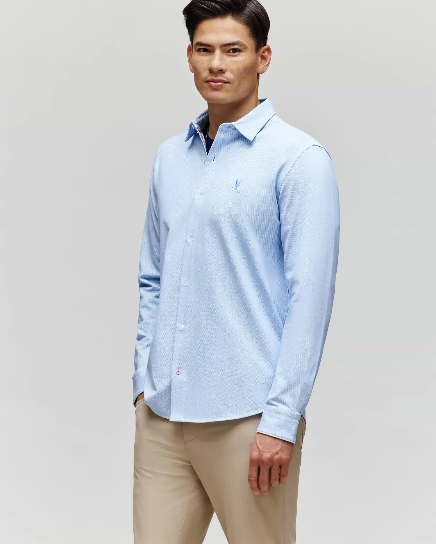 A man in the Psycho Bunny MENS JIM JERSEY STRIPED KNIT SHIRT (MT0300041), light blue, stands slightly turned with a neutral expression against a plain light background, paired with beige pants.