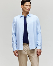 A man stands slightly angled against a plain light background, wearing the Psycho Bunny MENS JIM JERSEY STRIPED KNIT SHIRT (MT0300041) over a navy cotton jersey tee and beige pants.