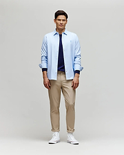 A man smiles while facing forward, wearing the Psycho Bunny MENS JIM JERSEY STRIPED KNIT SHIRT (MT0300041) over a navy tee, paired with beige pants and white high-top sneakers against a plain light background.