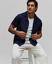 Navy blue Mens Josh Jacquard Shirt featuring a subtle tonal geometric pattern, relaxed fit, short sleeves, camp collar, and a small light blue Psycho Bunny logo on the bottom hem.