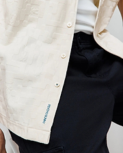 Mens Josh Jacquard Shirt in off-white, featuring a subtle textured jacquard pattern with integrated bunny skulls, white buttons, and a vertical blue Psycho Bunny embroidered logo on the hem.