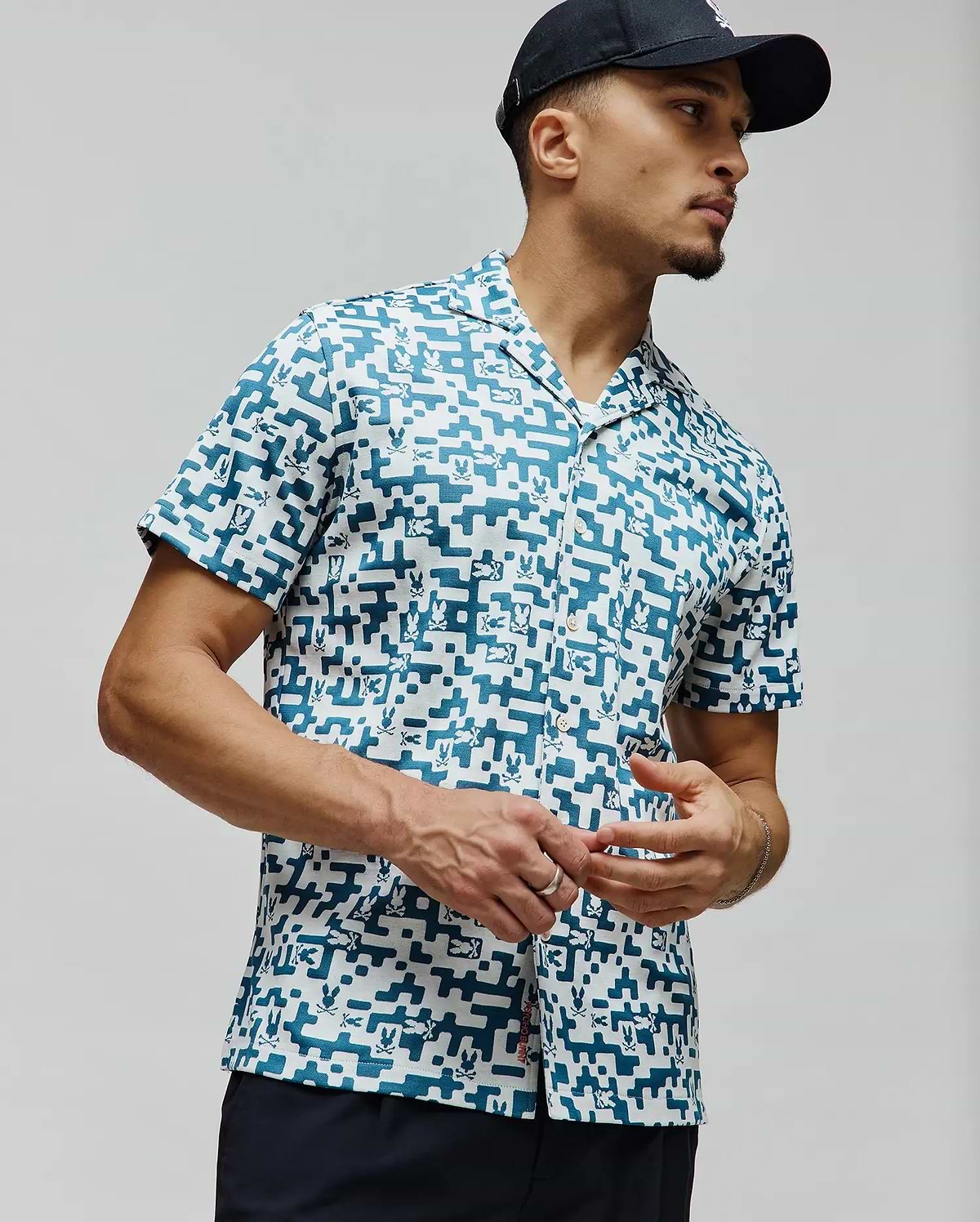 Mens Josh Jacquard Shirt, a relaxed fit white jacquard shirt with an all-over teal pixelated geometric pattern subtly incorporating small Psycho Bunny skull logos, finished with a camp collar.