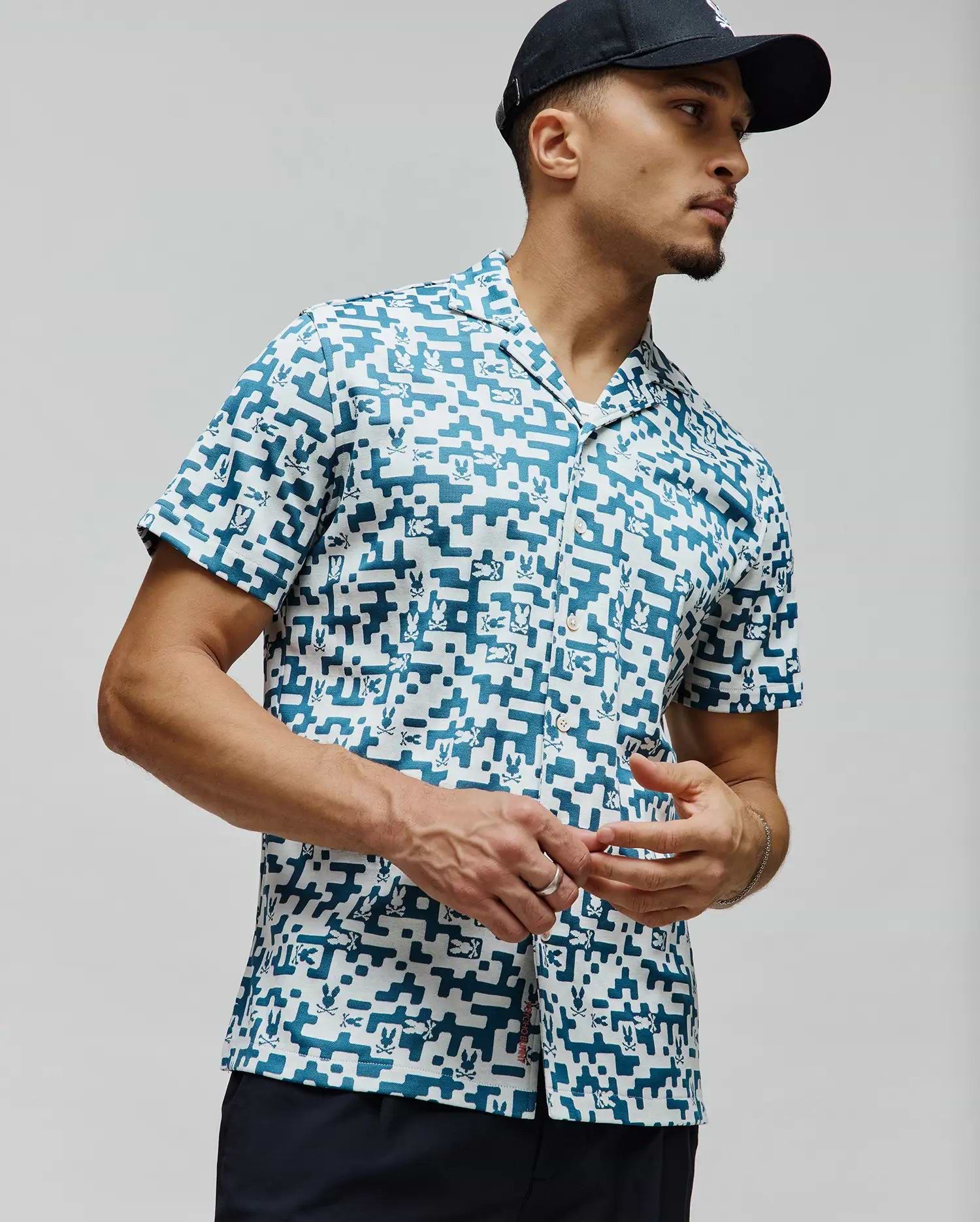 Mens Josh Jacquard Shirt, a relaxed fit white jacquard shirt with an all-over teal pixelated geometric pattern subtly incorporating small Psycho Bunny skull logos, finished with a camp collar.