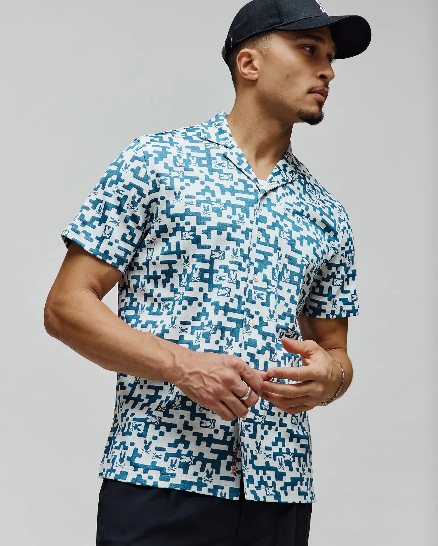 Mens Josh Jacquard Shirt, a relaxed fit white jacquard shirt with an all-over teal pixelated geometric pattern subtly incorporating small Psycho Bunny skull logos, finished with a camp collar.
