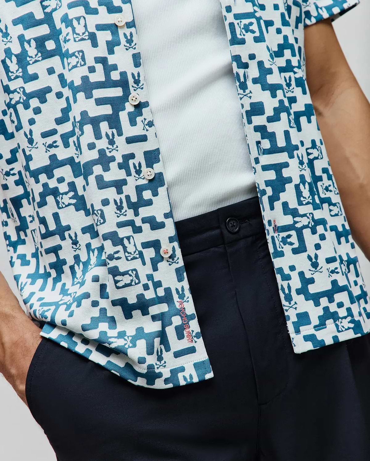 Mens Josh Jacquard Shirt, a relaxed fit short-sleeve button-up featuring a white and teal pixelated geometric pattern with repeated Psycho Bunny skull logos and subtle red placket branding.