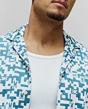 Mens Josh Jacquard Shirt, a white and teal jacquard short-sleeve shirt with an all-over geometric pattern and small Psycho Bunny skull logos, featuring a classic fit and camp collar.