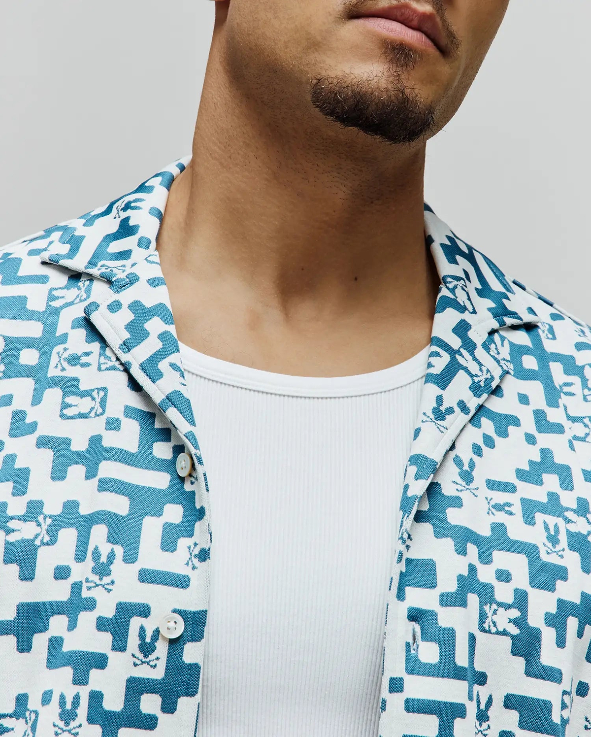 Mens Josh Jacquard Shirt, a white and teal jacquard short-sleeve shirt with an all-over geometric pattern and small Psycho Bunny skull logos, featuring a classic fit and camp collar.