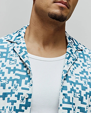 Mens Josh Jacquard Shirt, a white and teal jacquard short-sleeve shirt with an all-over geometric pattern and small Psycho Bunny skull logos, featuring a classic fit and camp collar.