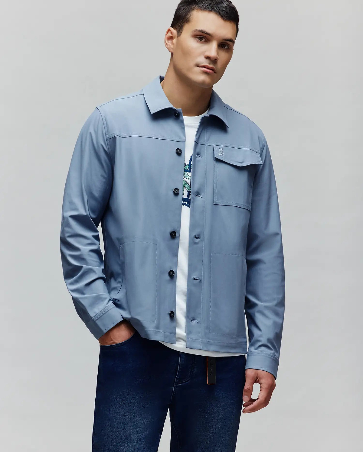 Mens Maverick Overshirt, a dusty blue classic fit overshirt with a smooth finish, black buttons, multiple patch pockets, and a small embroidered Psycho Bunny skull logo on the left chest pocket flap. (3)