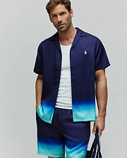 MENS DAX TENCEL SHIRT, a relaxed fit short-sleeve camp collar shirt featuring a navy blue to teal ombre gradient and a small embroidered Psycho Bunny skull logo on the left chest.