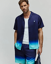 MENS DAX TENCEL SHIRT, a relaxed fit short-sleeve camp collar shirt featuring a navy blue to teal ombre gradient and a small embroidered Psycho Bunny skull logo on the left chest.