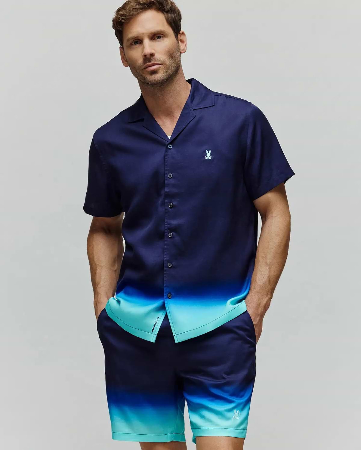 Mens Dax Tencel Shirt, a relaxed fit navy and aqua ombre short-sleeve button-up with a camp collar and small embroidered Psycho Bunny chest logo, paired with matching ombre shorts featuring a leg logo.