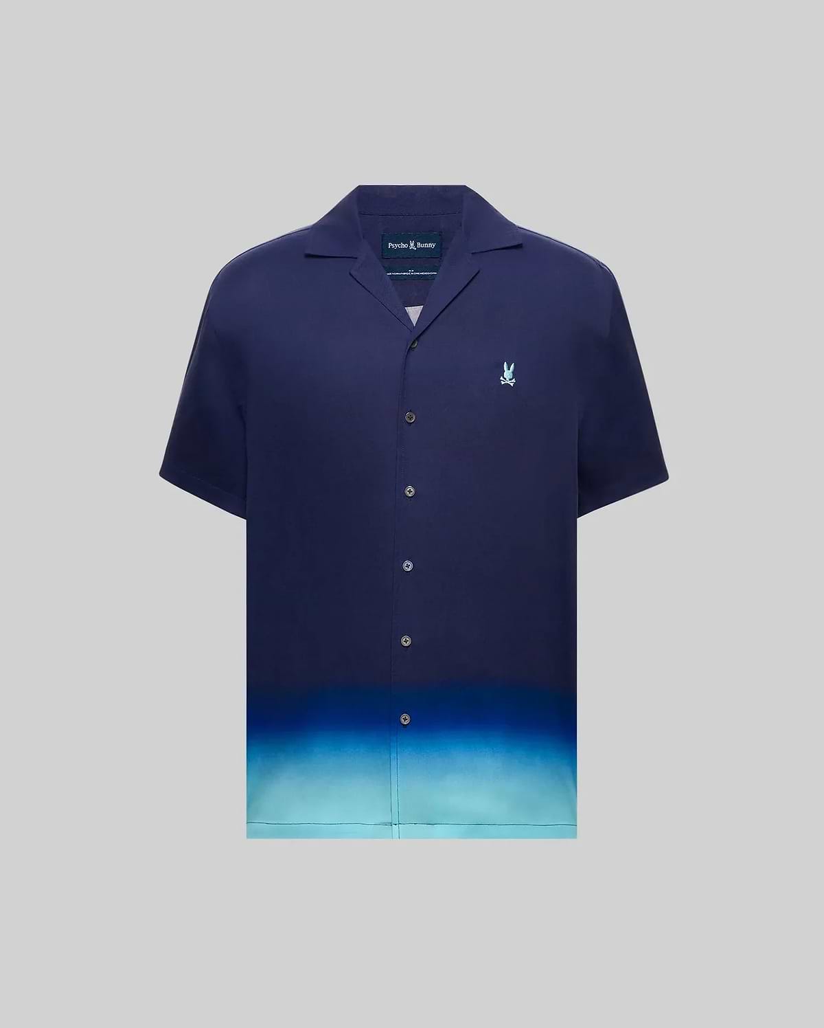 MENS DAX TENCEL SHIRT, a relaxed fit navy blue short-sleeve camp collar shirt with an ombre gradient fading to light blue at the hem and a small embroidered Psycho Bunny skull logo on the left chest.