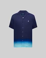 MENS DAX TENCEL SHIRT, a relaxed fit navy blue short-sleeve camp collar shirt with an ombre gradient fading to light blue at the hem and a small embroidered Psycho Bunny skull logo on the left chest.