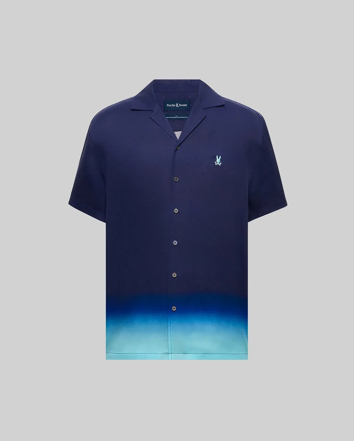 MENS DAX TENCEL SHIRT, a relaxed fit navy blue short-sleeve camp collar shirt with an ombre gradient fading to light blue at the hem and a small embroidered Psycho Bunny skull logo on the left chest.