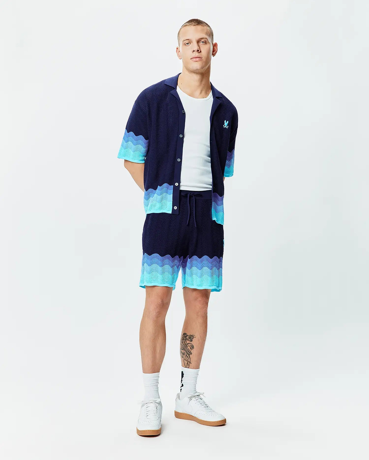 Mens Holden Oversized Knit Shirt and matching knit shorts, navy with wavy aqua and light blue gradient pattern. Oversized knit texture, small aqua embroidered Psycho Bunny skull logo on left chest.