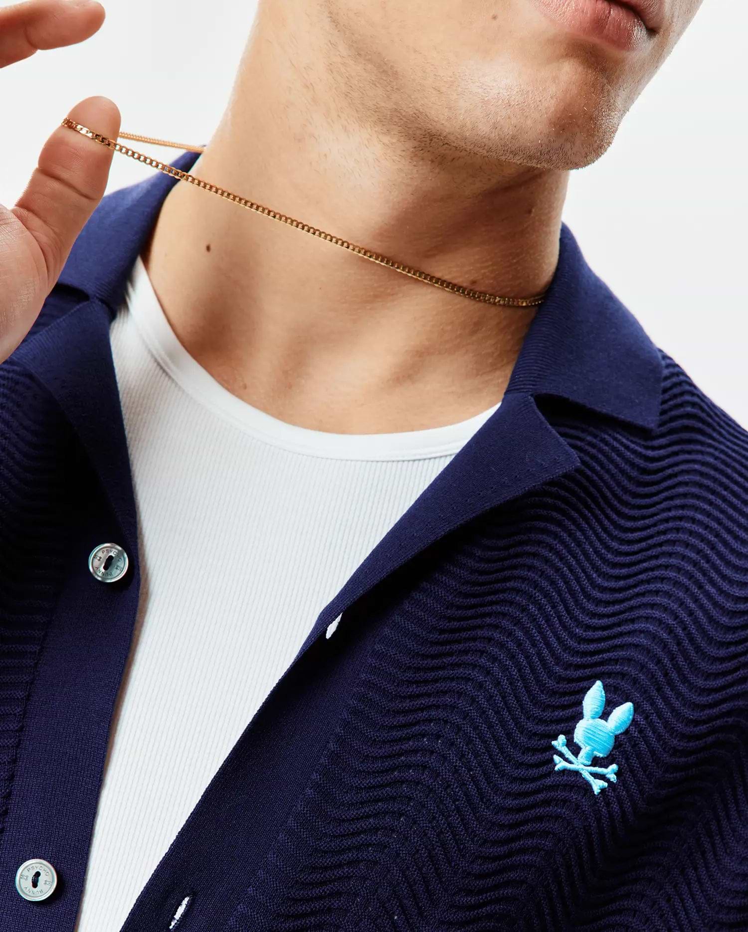 Mens Holden Oversized Knit Shirt in navy with a wavy knit texture, featuring a collared button-front, small light blue embroidered Psycho Bunny skull logo on the left chest, and branded buttons.