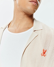 Mens Holden Relaxed Fit Knit Shirt, cream with a collared neckline and open-knit wavy texture, featuring a small embroidered orange Psycho Bunny skull logo on the left chest.